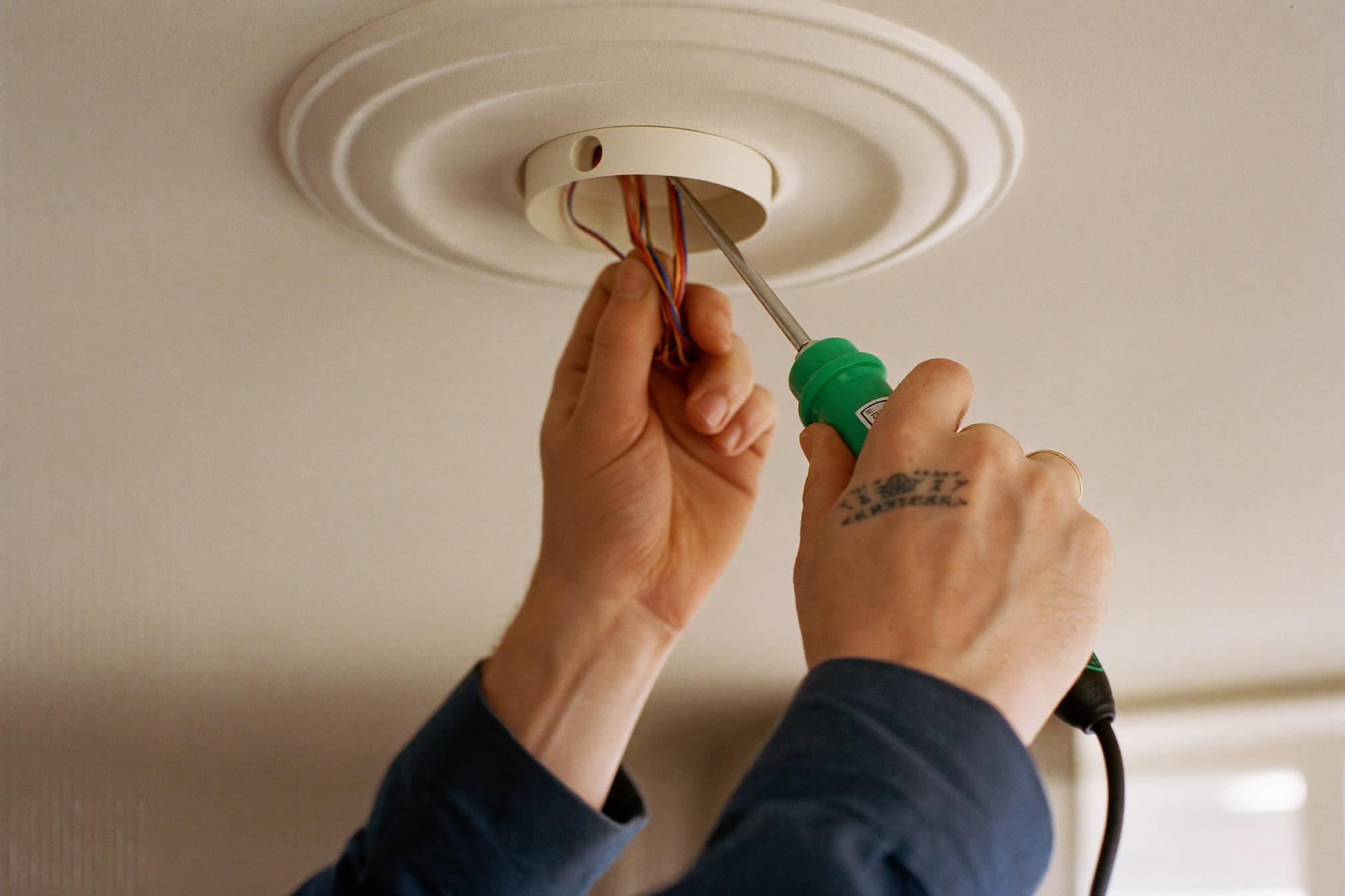 An electrician’s hands carefully wiring a ceiling light fitting in a UK home